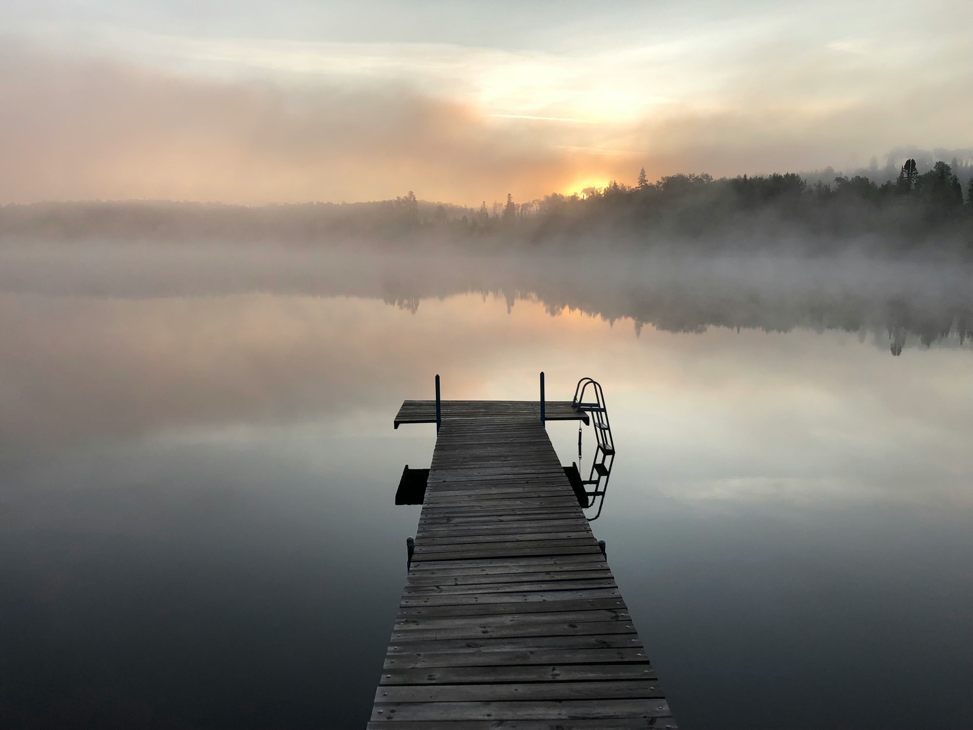 Misty lake at dawn with a quiet wooden dock